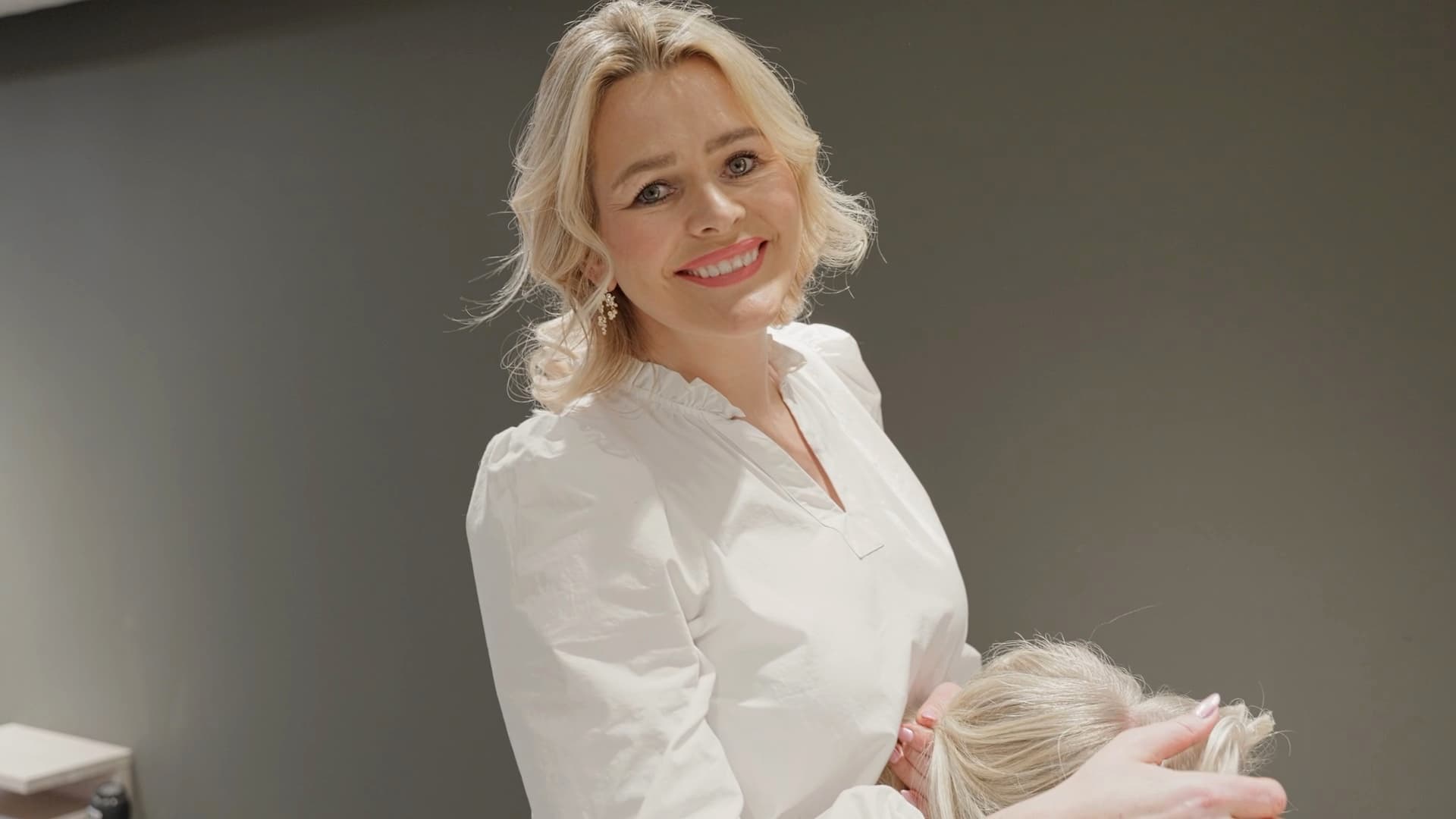 Frisør hos Ege·Børs ler mens hun klipper en kunde — bilde fra en produsert video